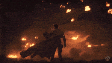 a man in a cape stands in front of a fire