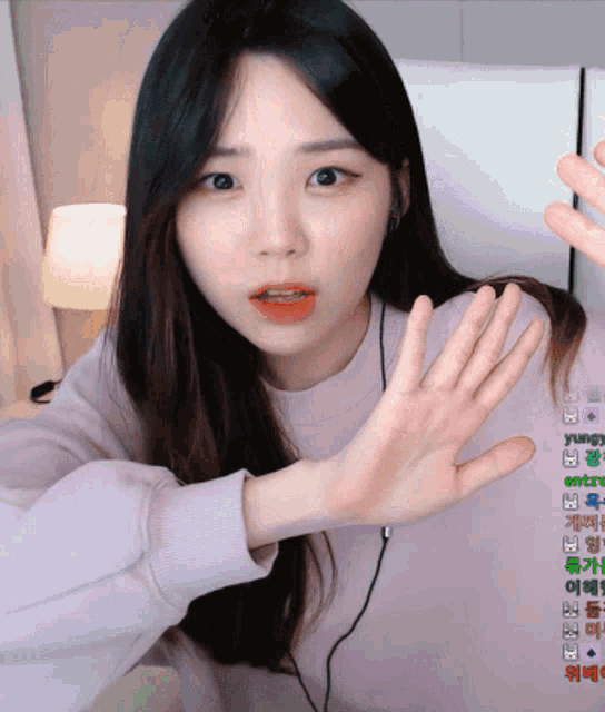 a girl in a pink sweater is waving her hand in front of a screen that says yungy