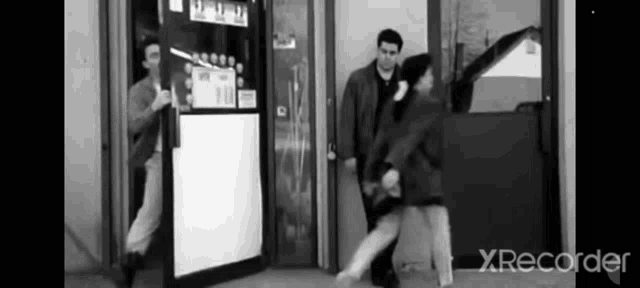 a black and white photo of a man standing next to a woman in front of a vending machine .