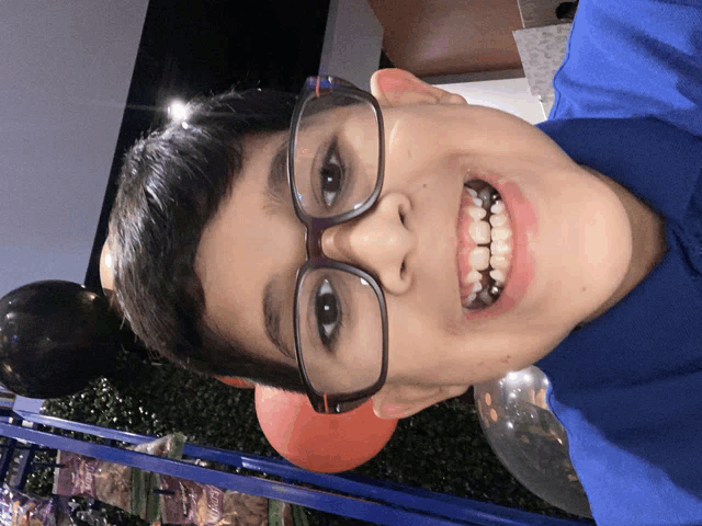 a boy wearing glasses and a blue shirt smiles