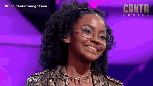 a girl wearing glasses is smiling in front of a purple background that says canta