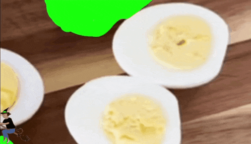three hard boiled eggs on a wooden table with a green screen behind them .