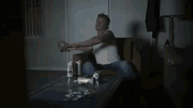 a man in a white tank top sits on a couch next to a table