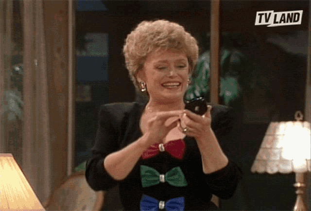 a woman is smiling while looking at her cell phone with a tv land logo in the corner
