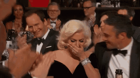 a woman in a black dress is covering her mouth while a man in a tuxedo applauds her .