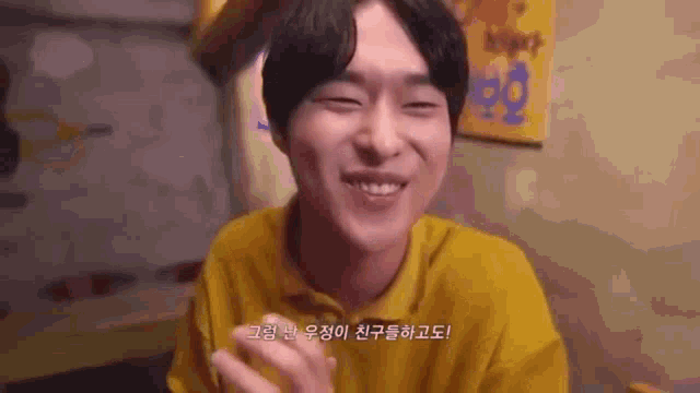 a man in a yellow shirt is smiling while sitting at a table in a restaurant .