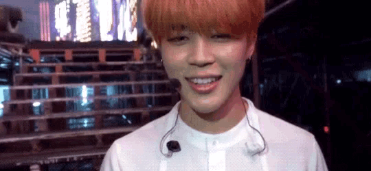 a young man with red hair is smiling and wearing a white shirt and earphones .