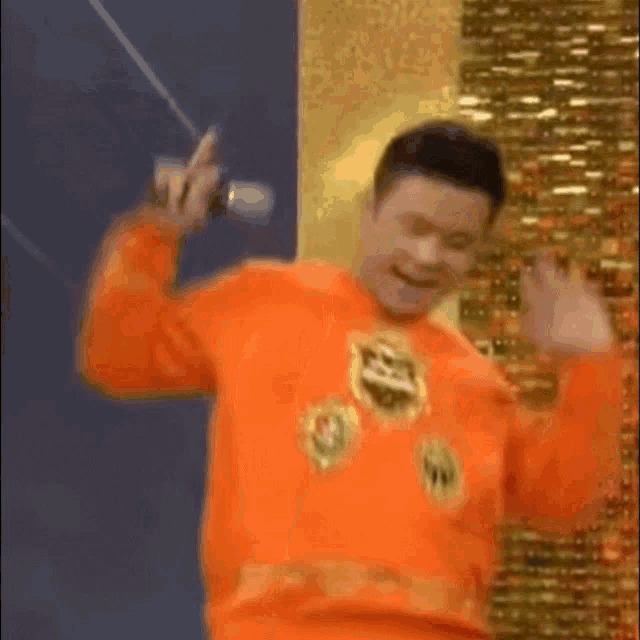 a man in an orange sweater is singing into a microphone while dancing .