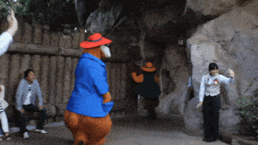 a man sitting on a bench takes a picture of a teddy bear in a blue jacket and red hat
