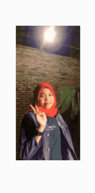 a woman wearing a red hijab and a blue jacket giving the peace sign