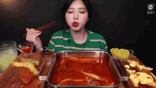 a woman in a green striped shirt is eating a tray of food with chopsticks