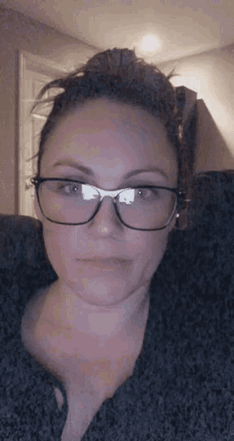 a woman wearing glasses looks at the camera with a serious look on her face