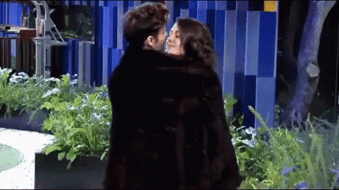 a man and woman are kissing in front of a blue building