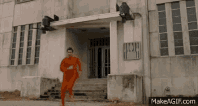 a man in an orange jumpsuit is running in front of a building that says ' jesus ' on it