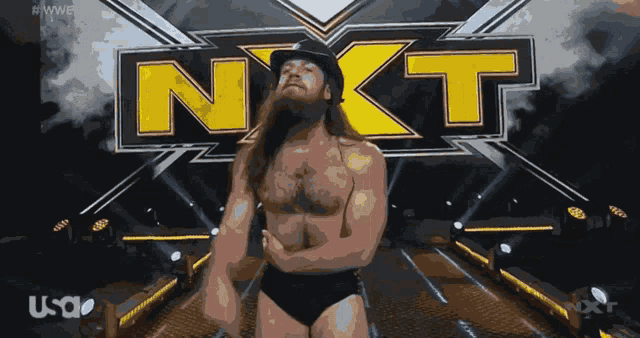 a bearded wrestler stands in front of a sign that says next