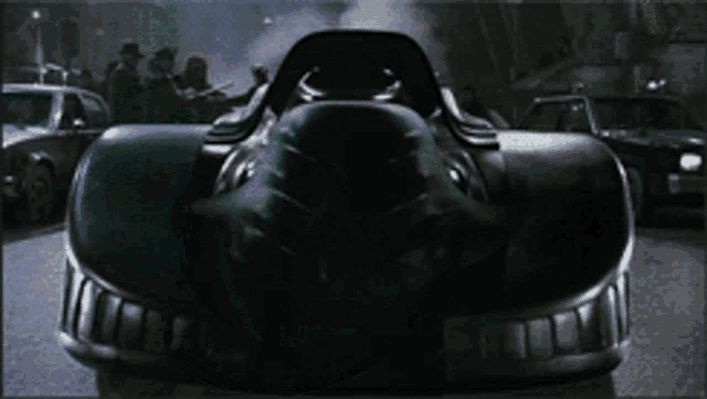 a black car is driving down a street in front of a crowd