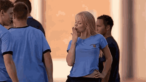 a woman in a blue t-shirt is blowing a kiss while standing in front of a group of people .