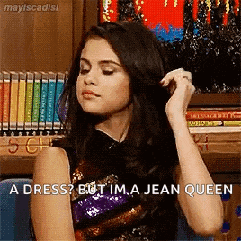 a woman is sitting in front of a bookshelf and talking about a dress