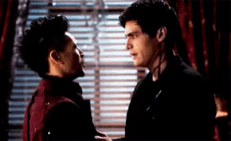 two men are standing next to each other in front of a window and looking at each other .