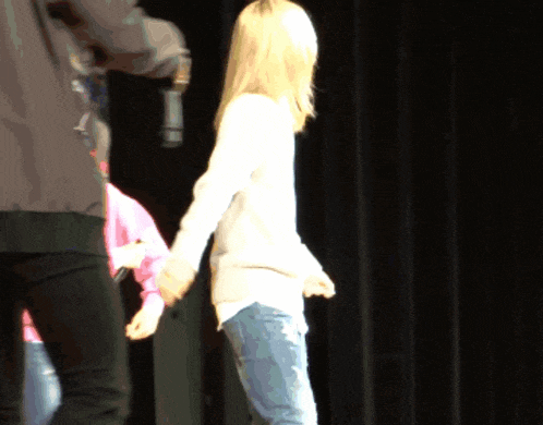 a woman in a white sweater stands on a stage holding hands with a man in a black jacket