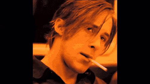 a man with long hair smoking a cigarette in a dark room