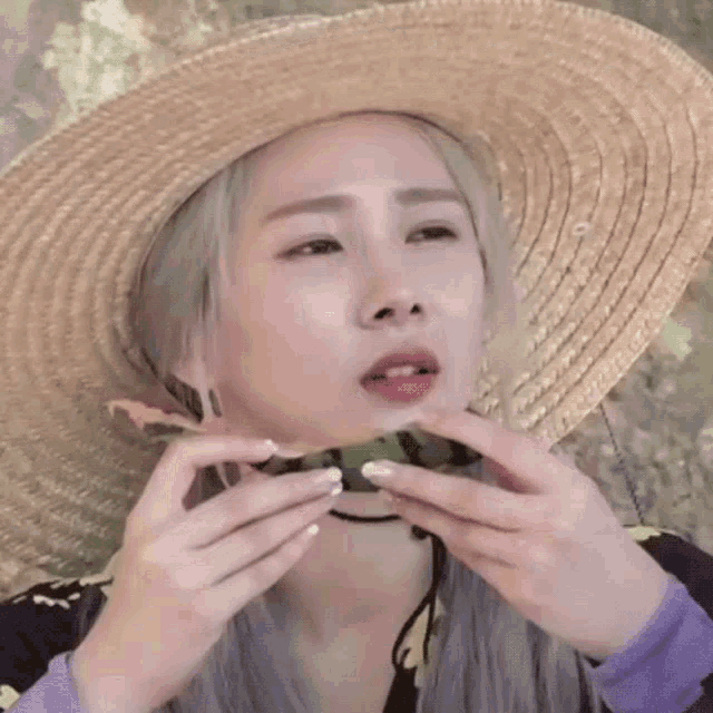 a woman wearing a straw hat is biting into a watermelon