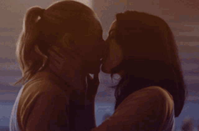two women kissing in a dark room with a ponytail