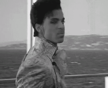 a black and white photo of a young man standing on a boat looking out over the ocean .