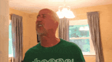 a man wearing a green shirt that says ' chanel ' on it stands in front of a window