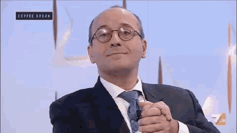 a man wearing glasses and a suit is sitting in front of a screen that says coffee break