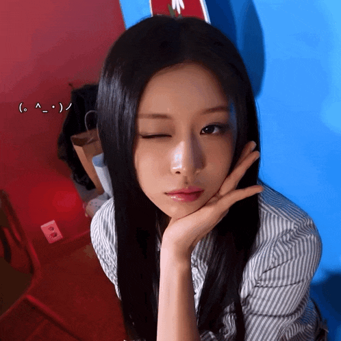 a woman with her hand on her face winks at the camera with a smiley face behind her