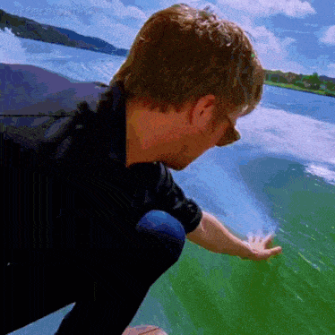 a man in a black shirt reaches out to touch a wave in the ocean