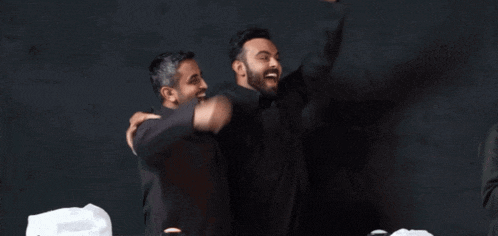 two men are standing next to each other laughing and hugging