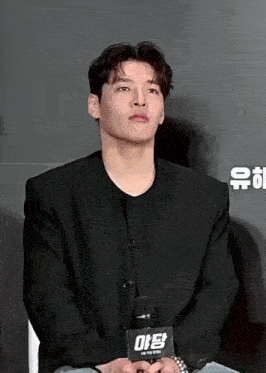 a man in a black jacket is sitting in front of a microphone with a sign that says ' ae ' on it