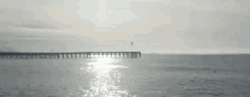a pier overlooking a body of water with the sun shining through the water .