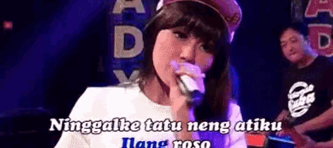 a woman is singing into a microphone on a stage with a man playing a guitar in the background .