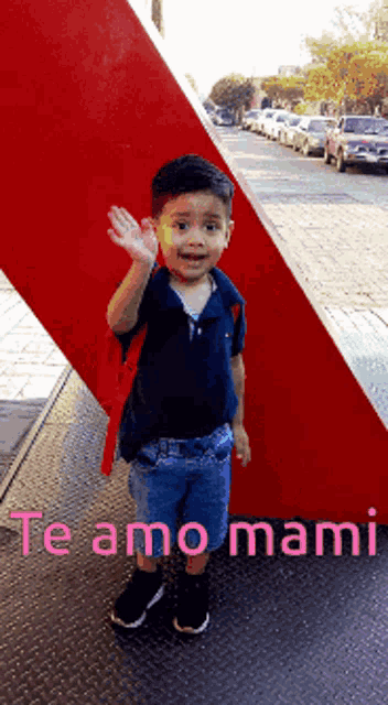 a young boy stands in front of a red sculpture with the words te amo mami written below him