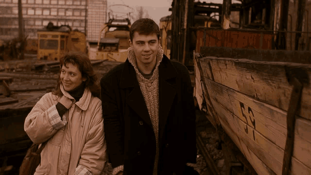 a man and a woman are standing in front of a wooden boat with the number 53 on it