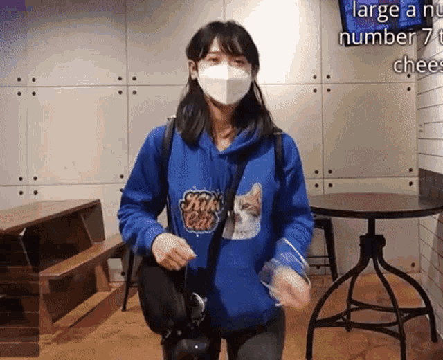 a woman wearing a mask and a blue sweatshirt with a cat on it