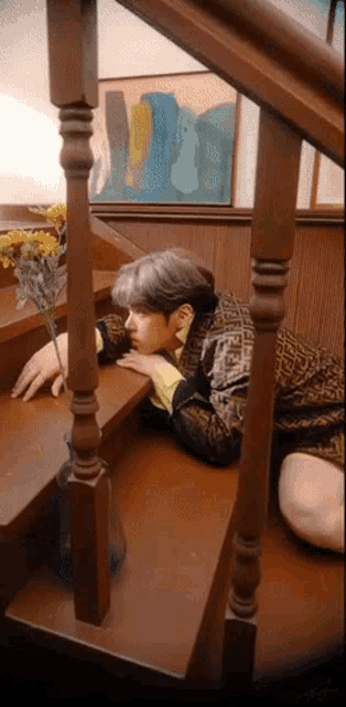 a person laying on a set of wooden stairs with a vase of yellow flowers