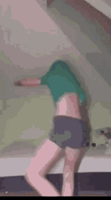 a woman in shorts and a green shirt is standing on a bed with her head in the air .