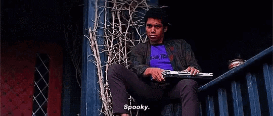 a man is sitting on a balcony with a laptop and a purple shirt .
