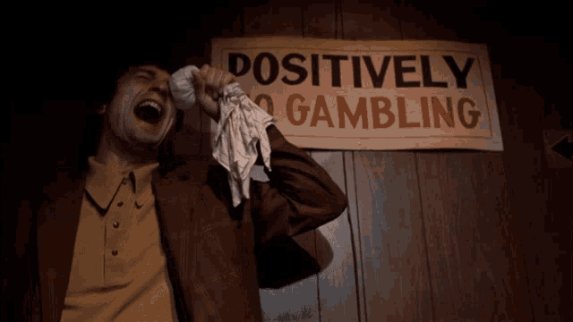 a man wipes his eyes in front of a sign that says positively no gambling