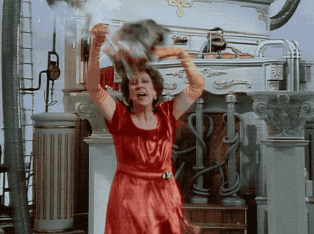 a woman in a red dress throws a bucket of water in the air in front of a building