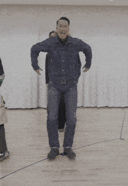 a man in a denim jacket and jeans is standing on a wooden floor