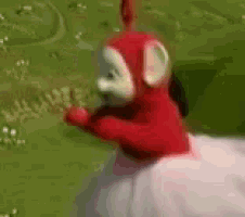 a red and white teletubbies teddy bear is standing in a grassy field .