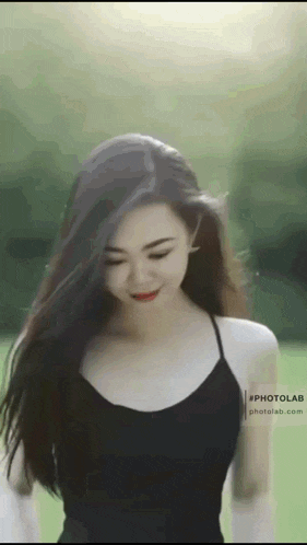 a woman in a black tank top is standing in a field with her hair blowing in the wind .