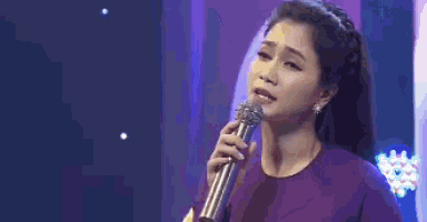 a woman is singing into a microphone while wearing a purple dress .