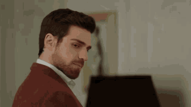 a man with a beard wearing a red suit and white shirt is standing in front of a lamp .