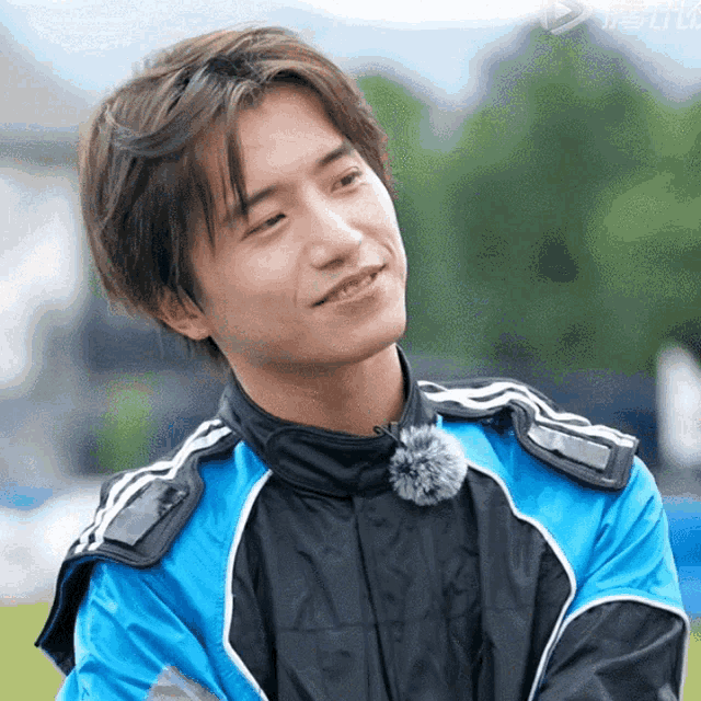 a young man wearing a blue and black jacket with a pom pom around his neck smiles